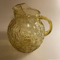 Amber glass pitcher with a heavily textured, rocky surface, rounded form, handle and spout visible from an angle showing overall shape and size.