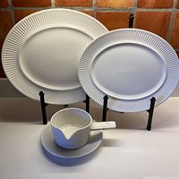 Set of three white ceramic serving pieces including two oval platters and a gravy boat on drip plate, displayed on stands and flat surface.