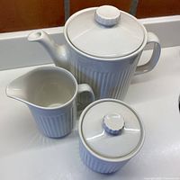 Photo showing the full 3-piece tea set: teapot, creamer, and sugar bowl, all white with vertical indentations.