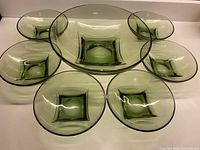 Seven olive green glass bowls set including one large serving bowl and six smaller bowls arranged on a white surface showing the square base design inside the bowls.