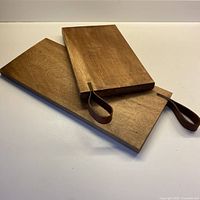 Two hand made wooden boards stacked, showing leather inset loop handles and wood grain on the surfaces