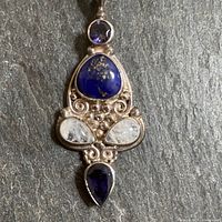 Close up view of pendant stones and detailed silver frame showing lapis lazuli, amethyst, and moonstones with textured spheres and swirl designs.