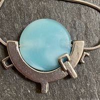 Close up of front of necklace pendant showing round blue synthetic stone in pewter base with industrial mechanical design.