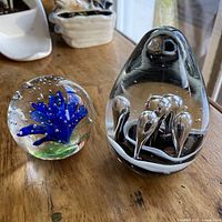 Photo showing both paperweights side by side on wooden surface highlighting size and design differences.