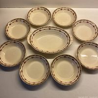 Overview of 8 round fruit nappies arranged around 1 oval handled dish, all decorated with rose and cherry floral motifs.