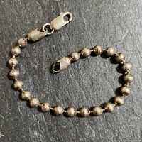 Full view of the silver bead bracelet laid flat showing lobster clasp and bead chain on dark surface.