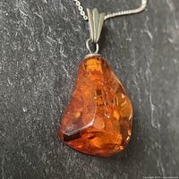 Close-up view of large polished amber stone with sterling silver cap showing inclusions inside the amber.