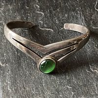 Vintage Mexican sterling silver cuff bracelet shot from front showing green semi-precious stone and cut-out chevron design.