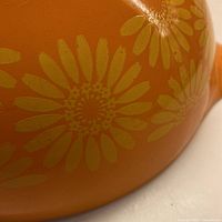 Close-up of yellow sunflower design on orange PYREX bowl.