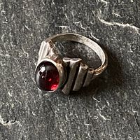 Side angle view of vintage sterling silver ring showing the deep cherry red oval semi-precious stone and the geometric indented design on the band.