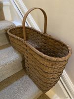 Woven basket hanging on carpeted stairs showing full profile and handle.