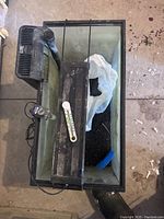 Top view of rectangular aquarium showing pump, heater, thermometer, lighting fixture, artificial substrate and decorations inside.