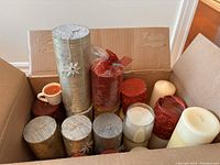 Box of assorted pillar and votive candles showing silver, red, white, and brown colored candles in various shapes and sizes