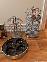 Two chrome metal coffee pod holders and a round stove-top egg poacher with four compartments and black handle