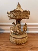 Front view of the ivory and gold musical carousel figurine with horse figures and floral patterns.