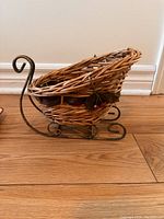 Side view of small brown wicker sleigh with curled metal runners and holly leaf decoration