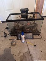 Front view of complete aquarium setup showing tank with filter, heater, decorations, LED light bar, and aquarium supplies on floor
