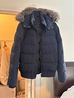 Front view of navy blue Tommy Hilfiger down fill bomber coat with fur-trimmed hood hanging on a hanger.