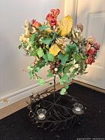 Full view of the steel flower bouquet stand holding a mixed artificial flower arrangement with green leaves, cream, red and yellow flowers. The stand has 4 tea light candle holders.