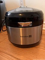 Closed view of the Kuraidori electric smart cooker showing stainless steel body with brand mark.