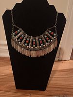 Silver-tone statement necklace with red stones and feather-like pendants on large black bust display, showing detailed design