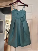 Front view of aquamarine junior bridesmaid dress showing pleated bodice, double shoulder straps and flower detail on waist.