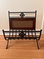 Front view of metal and wood magazine rack showing woven inset and scroll detail
