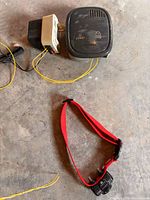 Photo of the home base unit with power adapter and red collar receiver lying on concrete floor.