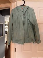 Front view of Roxy fall coat hanging on door, showing the hood, zipper, pockets, and sleeves with adjustable wrist cuffs.