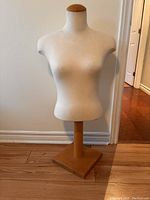 Front view of the fabric-covered mannequin torso on a wooden base stand, showing realistic female body shape and beige fabric covering.