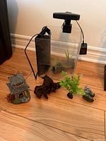 Clear rectangular aquarium tank with black overhead light and power cord, displayed on wooden floor against wall.