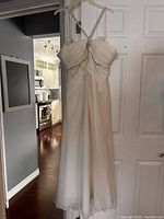 Front view of white wedding dress hanging on a door showing pleated bust with lace details and knotted strap design.
