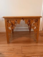 Side view showing intricate leaf and vine cutout design on table legs and apron.