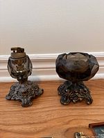Vintage WW1 army and navy style lighter on ornate metal base with matching faceted glass ashtray with same style base, both sitting on wooden surface