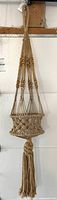 Entire vintage boho macrame plant hanger hanging vertically, showing full length and braided tassel.