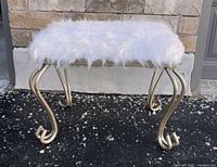 Front angle view of small rectangular stool showing white fluffy Icelandic sheepskin wool uphostery and rustic hand-forged iron curled legs.