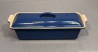 Front and top angled view of blue Le Creuset terrine with attached cream ribbed handles and lid with central handle.