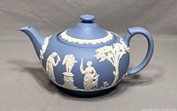 Side view of vintage Wedgwood jasperware blue teapot with white classical relief decorations and lid on, showing spout and handle.