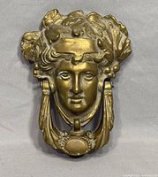 Full view of brass door knocker with human face and leaf motif