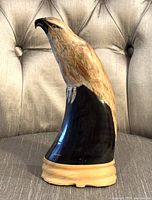 Front side view of the hand carved buffalo horn eagle/falcon sculpture on carved wood base showing the detailed wood carved head and glossy finish horn body with natural wood base.
