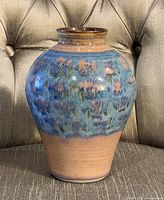 Front view of a bulbous pottery vase with blue and brown glaze sitting on a chair.