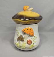 Front view of vintage Laurentian Pottery mushroom canister with detailed mushroom decorations on white base.