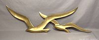 Full view of the three brass flying birds wall sculpture mounted on a gray cloth background showing size and shape.