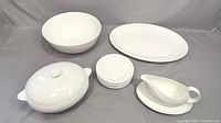 Overview of all white dinnerware pieces: large bowl, oval platter, lidded bowl, stack of dessert plates, gravy boat and tray.