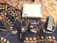 Xbox 360 console with power adapter, cables, and wired controller tangled around it on patterned carpet.