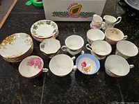 Overview of set showing 10 cups, 10 saucers, and 2 small creamers arranged on dark countertop.
