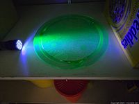 Top view of the round uranium glass cake plate showing embossed floral design and fluorescent glow under UV light.