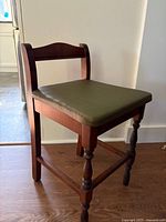 Side view of 1930s vintage solid wood chair showing turned legs and stretcher supports with green vinyl seat.
