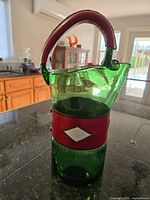 Side view of green glass cocktail pitcher with red leather handle and central leather band on kitchen counter.