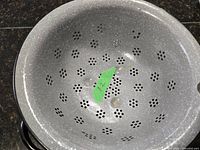 Top-down view of the inside of the graniteware colander showing flower-shaped perforations and speckled gray enamel interior.